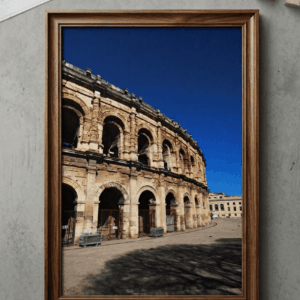 Photographie encadrée dans un cadre en bois, représentant l'amphithéâtre romain des Arènes de Nîmes sous un ciel bleu intense. Photo d'art par BTarts.